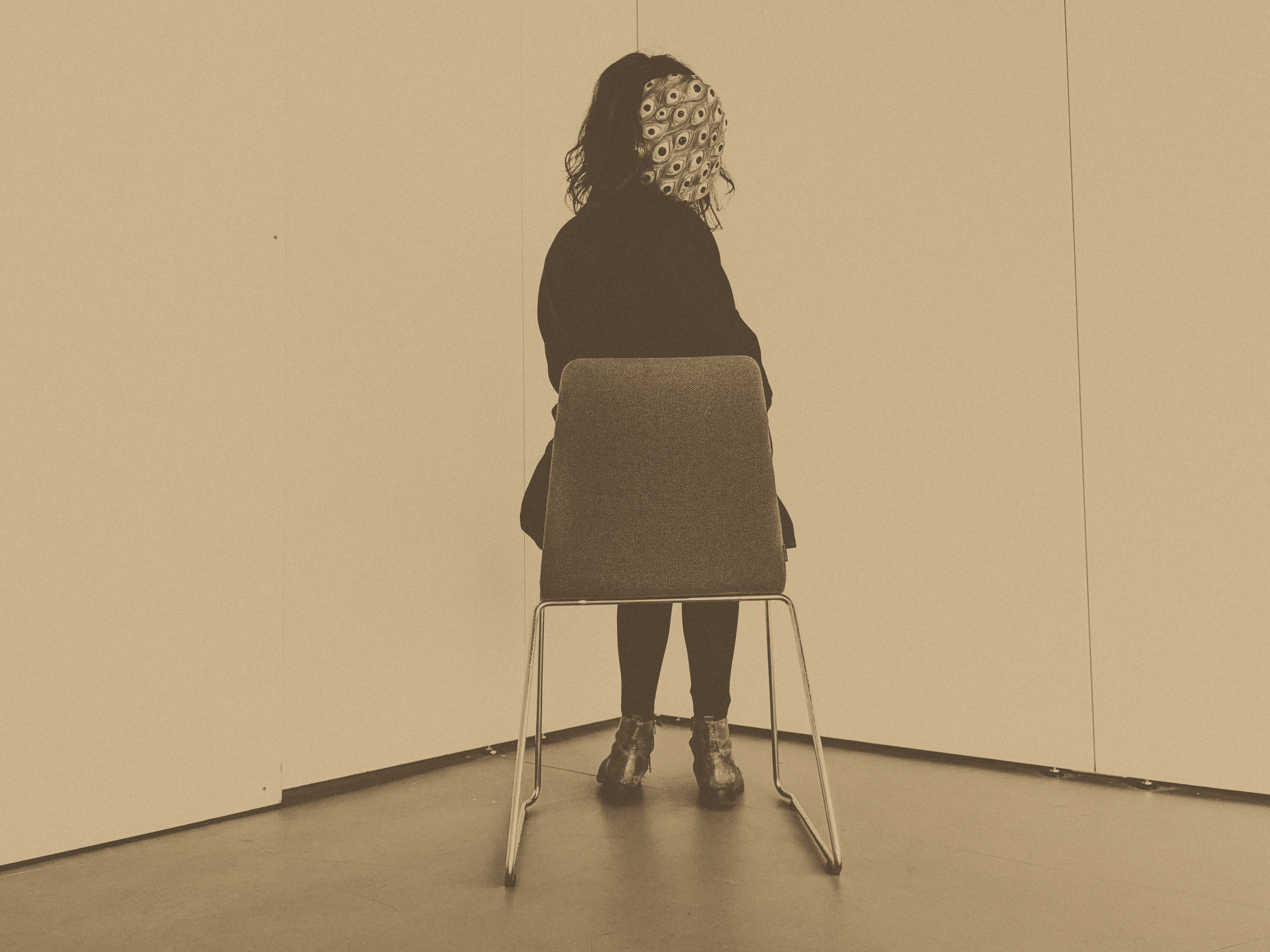 victorian style photograph of a woman sat, wearing a mask covered in eyes facing the camera