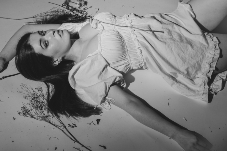 a black and white photograph of a woman led against a white background surrounded by flowers
