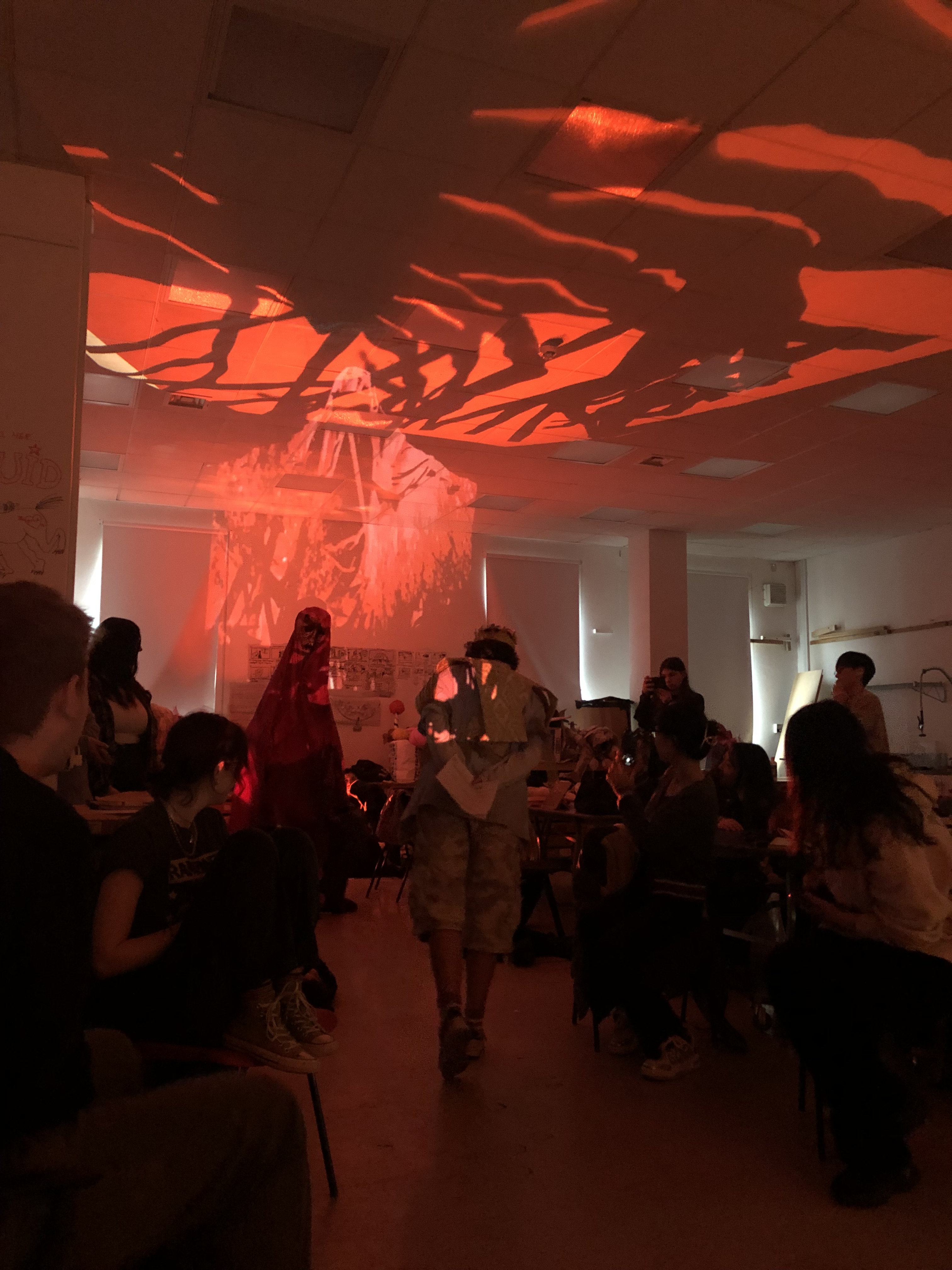 photograph of a stage performance, with a focus on the red, shadowed tree like lighting on the ceiling